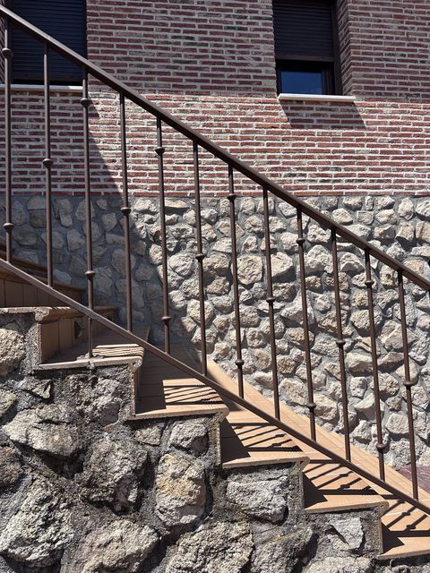 Barandilla de forja marrón en escalera exterior de piedra